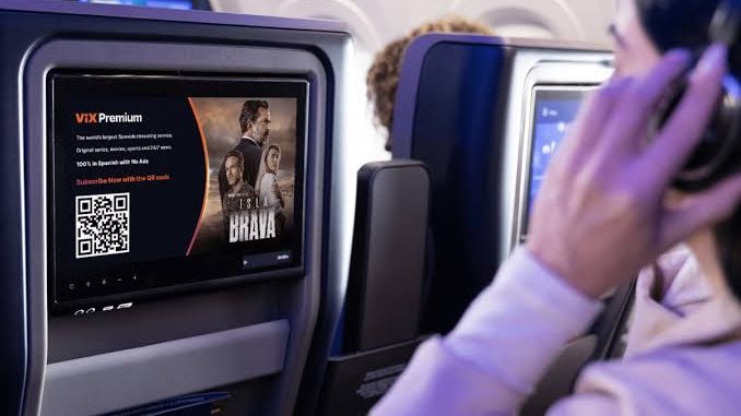 Passenger in headphones watching an aircraft seatback screen showing a ViX Premium streaming ad with a QR code
